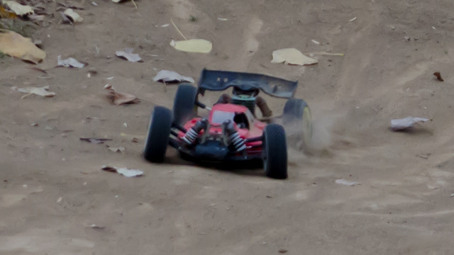 Image of an HotBodies nitro-fueled buggy squatting low between small jumps